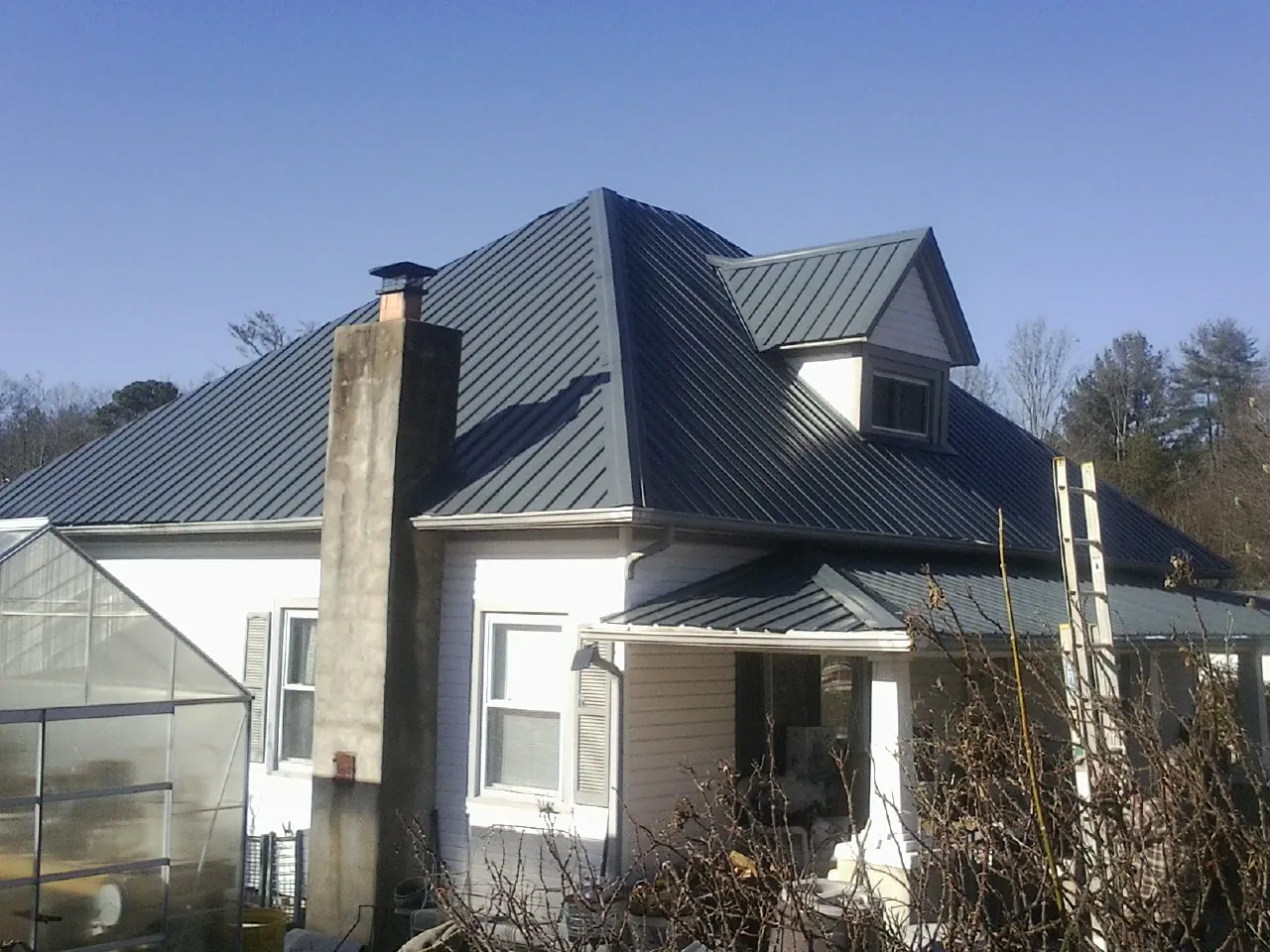 Dark blue standing seam metal roof on a white farmhouse with dormer — Slate & Tile Roof Repair by Roofing Brothers in Wanamingo