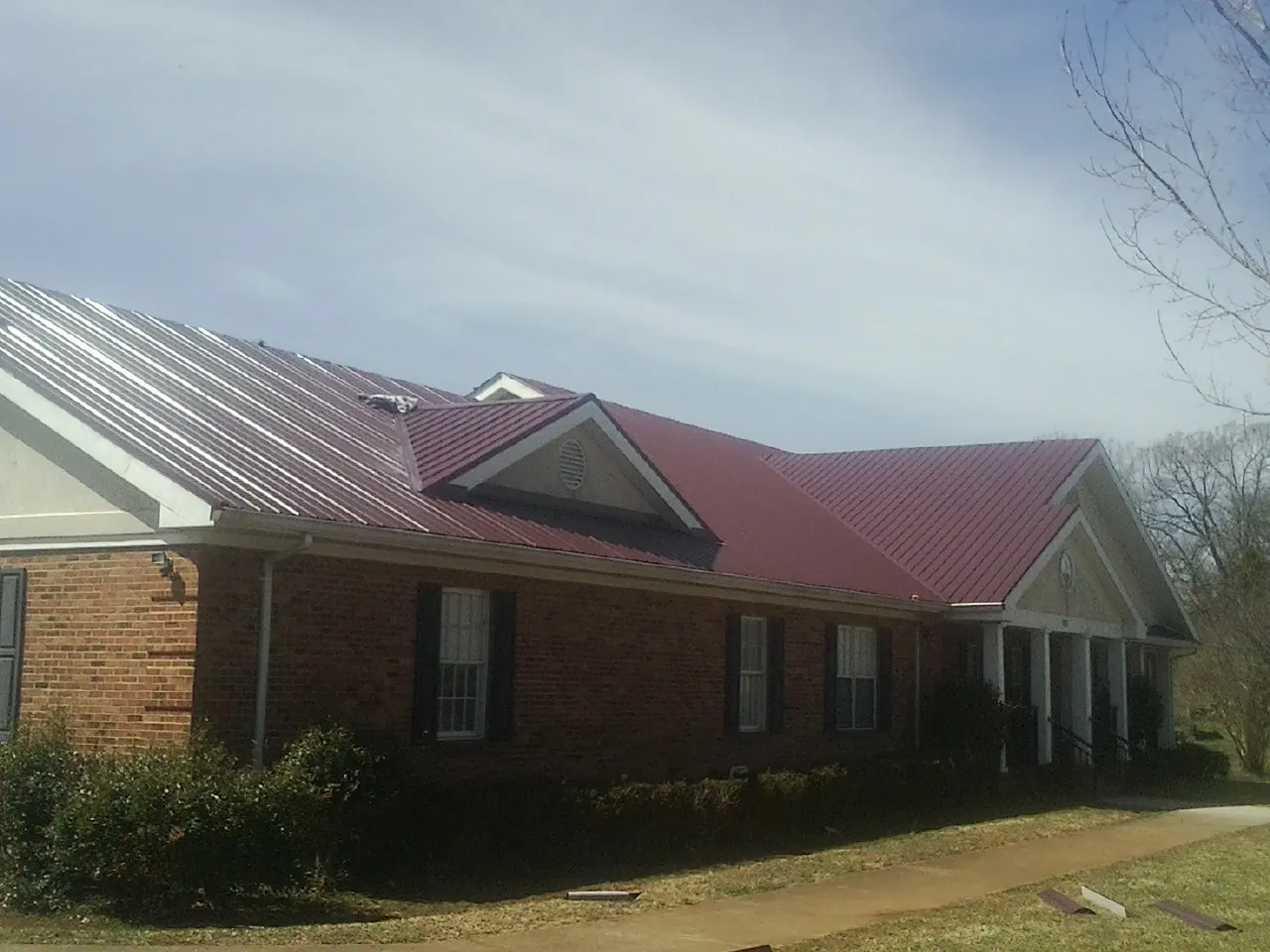 Red metal roof with gabled entries on a long brick building, from a Hail Damage Roof Repair job in Wanamingo