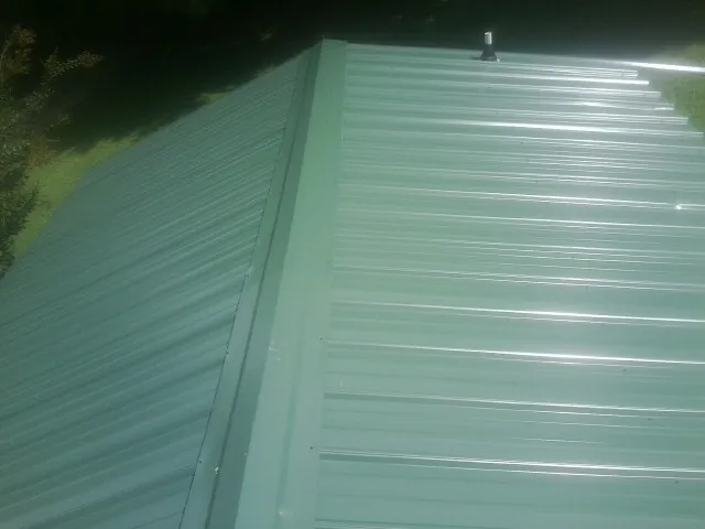 New green metal panels meeting at the ridge of a roof — Flat Roof Repair work by our crew in Wanamingo