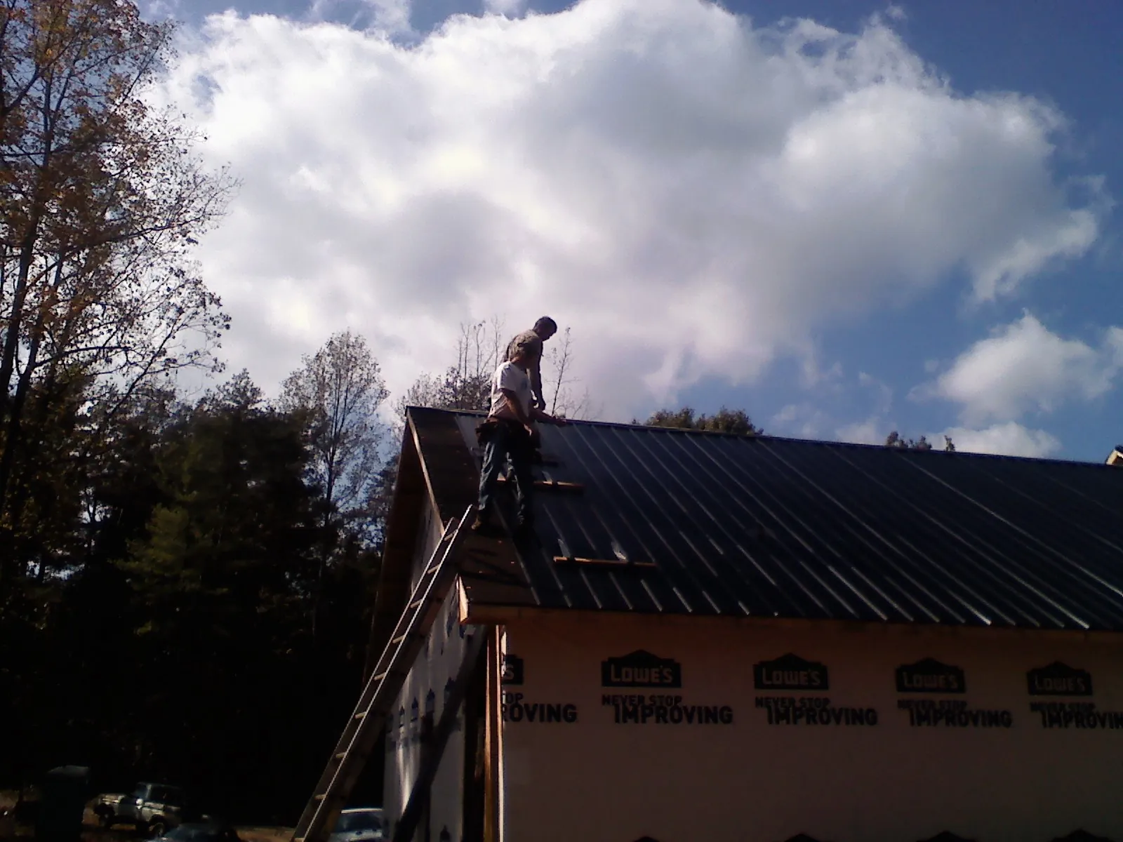 Roofer fastening dark metal panels high against a cloudy sky, from a Roof Inspection job in Wanamingo