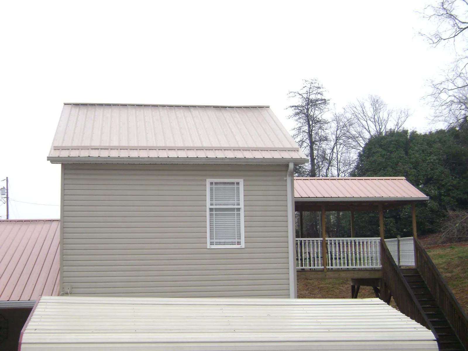 Tan metal roofs on a two story addition and attached porch, from a Roof Replacement job in Wanamingo